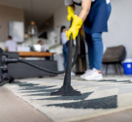 Close-up on a professional cleaner vacuuming a carpet while working at an apartment - housework concepts